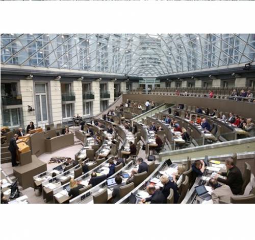 Sitzungssaal des Flämischen Parlaments in Belgien. Ein Glasdach überspannt einen Innenhof, darin sind die Sitze & Tische wie ein Hörsaal angeordnet.