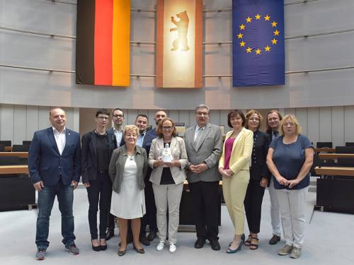 Gruppenfoto im Plenarsaal mit Ralf Wieland. In der Mitte steht eine Frau, die eine Trophäe in Form des Berliner Bären hoch hält.