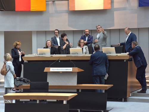 Mehrere Menschen stehen um den Sitz des Präsidenten im Plenarsaal. Ralf Wieland zeigt auf etwas. Eine Frau sitzt auf seinem Stuhl.