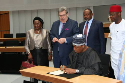 Ein nigerianischer Mann sitzt an einem Tisch im Plenarsaal und unterschreibt eine Urkunde. Weitere Männr und eine Frau aus Nigeria sowie Ralf Wieland stehen um ihn herum.