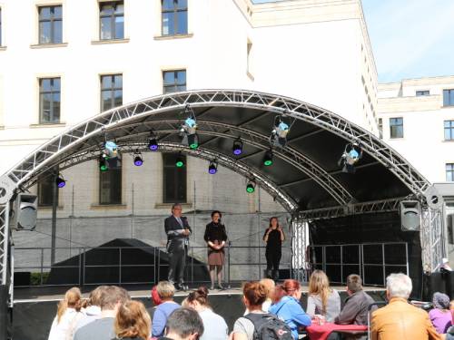 Hoffest mit Bühne und gebogenen Dach, 3 Personen auf der Bühne, vorne Zuschauer
