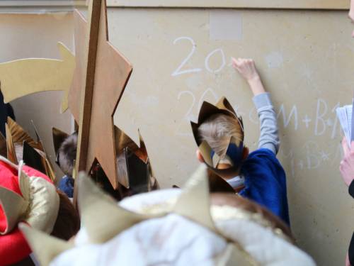 Schüler mit goldenen Papierkronen schreiben einen Segen zum Tag der Heiligen drei Könige
