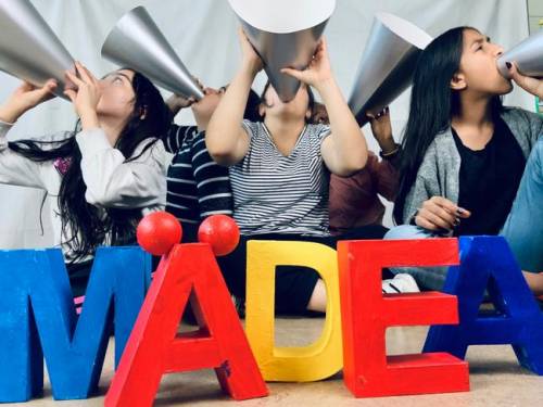 Eine Gruppe Mädchen halten Sprachrohre aus Pappe an den Mund. Vor ihnen stehen Buchstaben und bilden das Wort "MÄDEA"