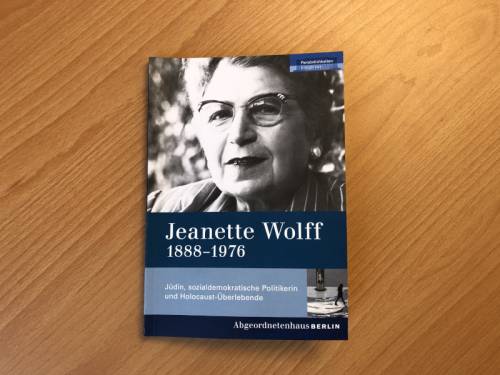 Eine gedruckte Broschüre über Jeanette Wolf, die auf einem Holztisch liegt