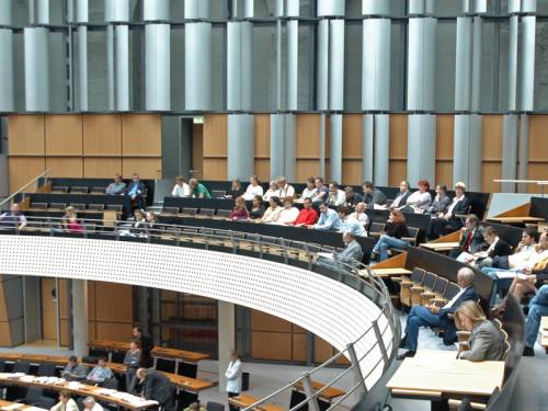 Besucherinnen und Besucher sitzen auf der Tribüne. Man sieht ein paar Abgeordnete im Plenarsaal.