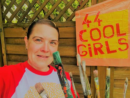 Frau steht mit Pinseln vor einem Schild auf dem steht "44 Cool Girls"