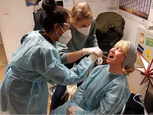 Zwei Frauen mit Maske schauen einer anderen Frau für eine Untersuchung in den Mund