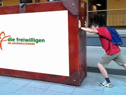 Ein Mann schiebt einen überdimensioniert großen Koffer mit der Aufschrift "die freiwilligen"
