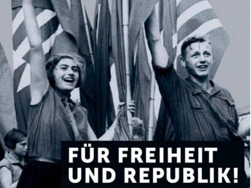 Die Fotografie zeigt zwei Jugendliche an einer Fahne, sie strecken jubelnd und in Aufbruchstimmung ihre Hände in die Luft