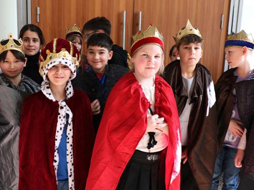 Gruppenfoto von Schülerinnen und Schüler während des Demokratiespiels. Alle tragen königliche Umhänge und Kronen.